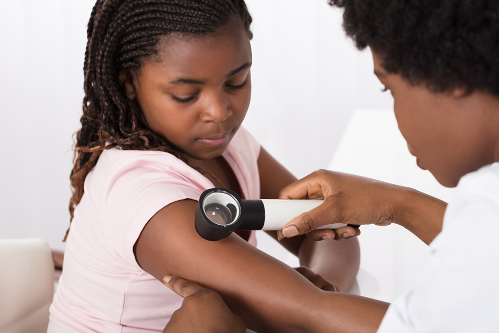 Ärztin untersucht Haut von Mädchen mit Dermatoskop.