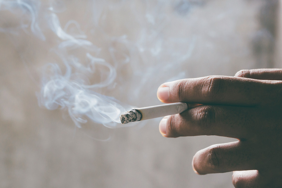 Eine brennende Zigarette steckt zwischen zwei Fingern. Thema: Krebs vorbeugen