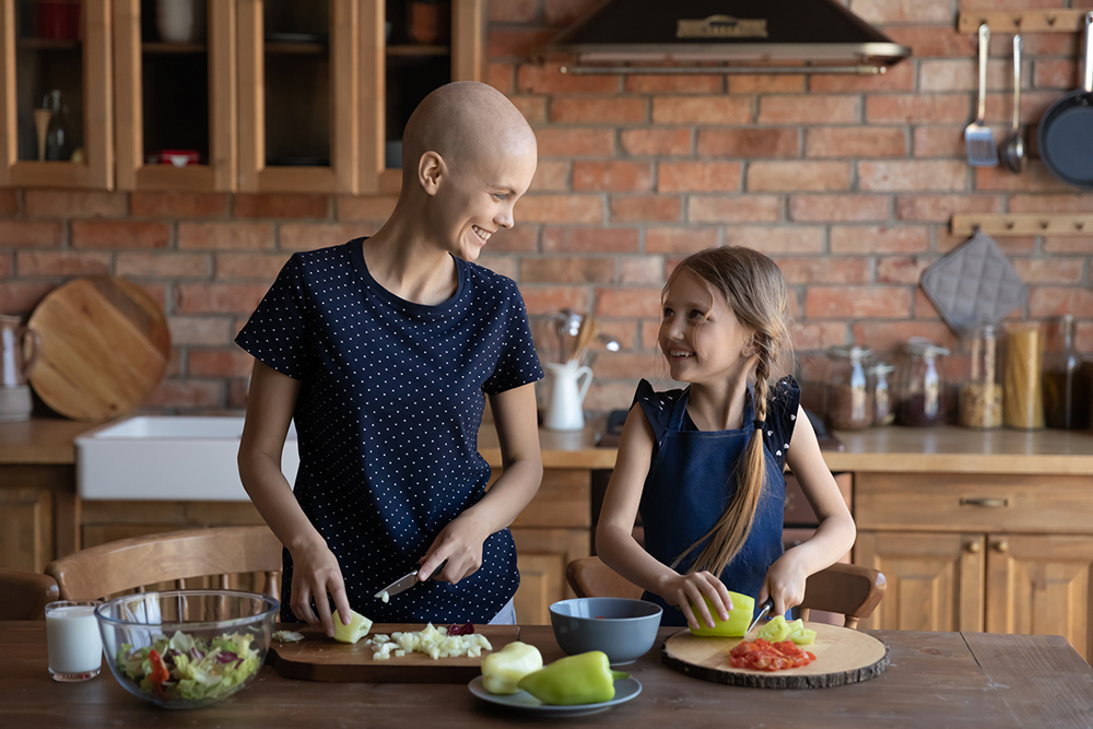 Glückliche kranke Mutter Krebspatientin und kleine Tochter kochen zusammen.
